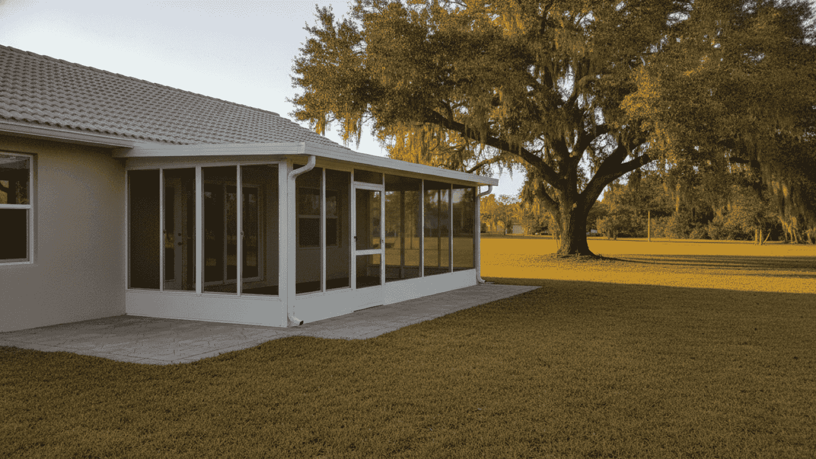 White aluminum screened enclosure under the existing tile roof of a Polk County home, over a paver patio with a live oak beyond
